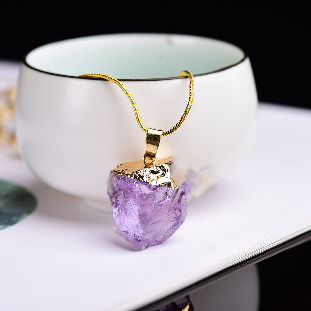 Amethyst pendant necklace with gold chain on a white surface