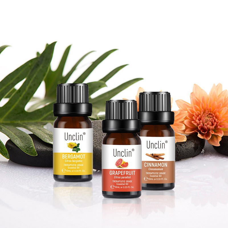 Three Unclin essential oil bottles with labels on a white surface with green leaves and a flower in the background.