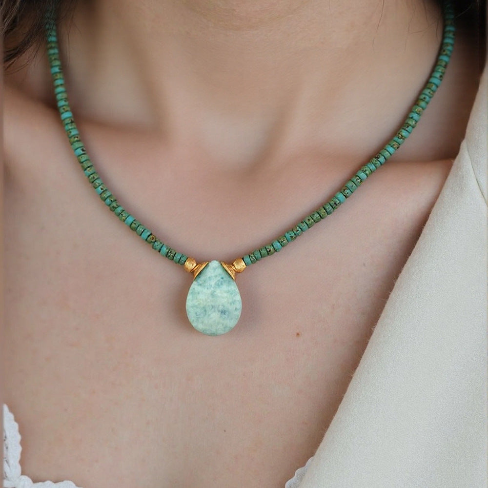Necklace with green beads and a teardrop-shaped pendant on a person wearing a white lace top.
