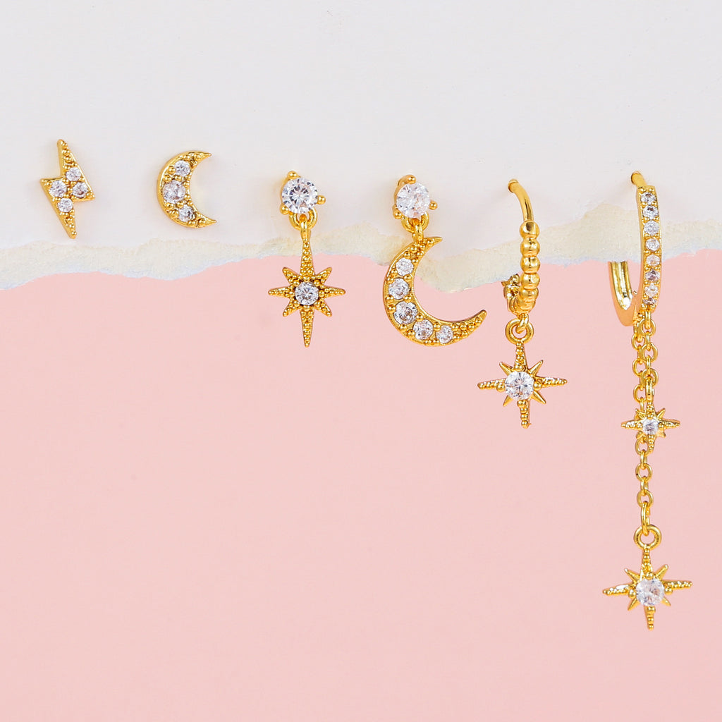 Gold earrings with star and moon designs on a pink and beige background