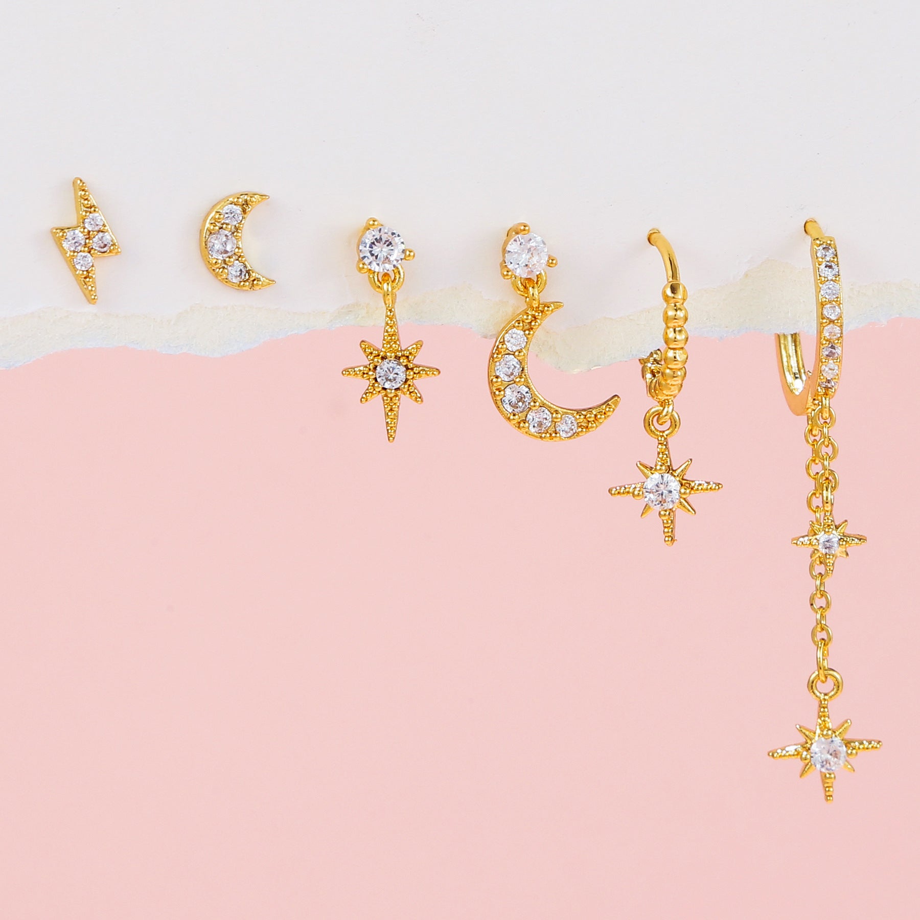 Gold earrings with star and moon designs on a pink and beige background