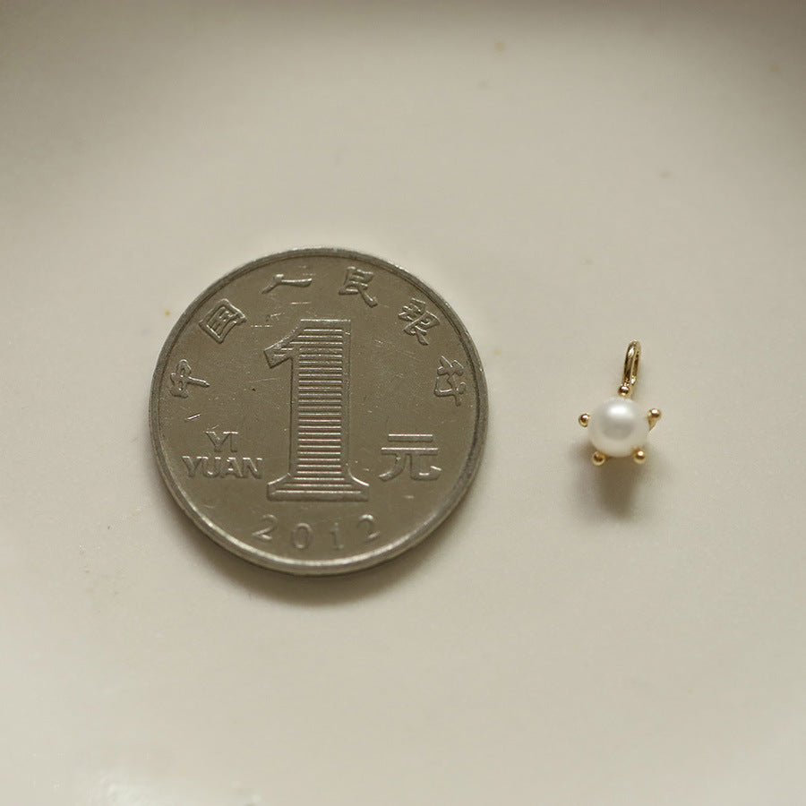 Gold pearl pendant next to a Chinese yuan coin on a beige background