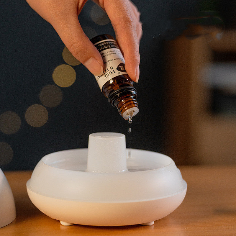 Hand pouring essential oil into a diffuser with a blurred background