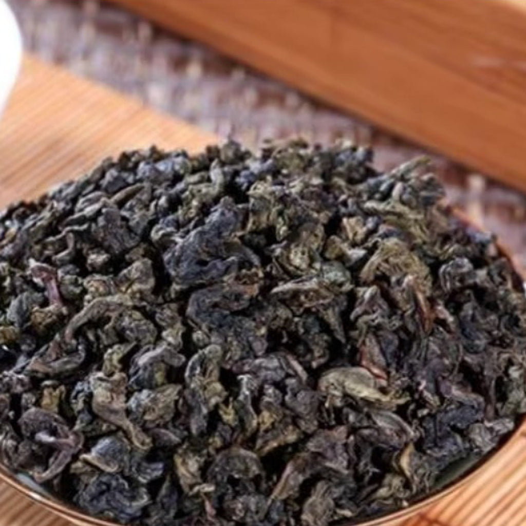 Dry green tea leaves in a wooden bowl on a wooden surface