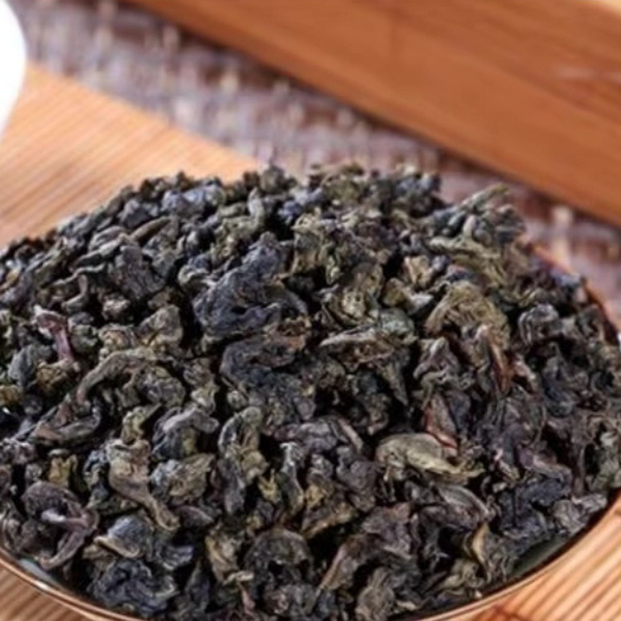 Dry green tea leaves in a wooden bowl on a wooden surface