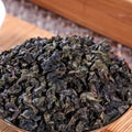 Dry green tea leaves in a wooden bowl on a wooden surface