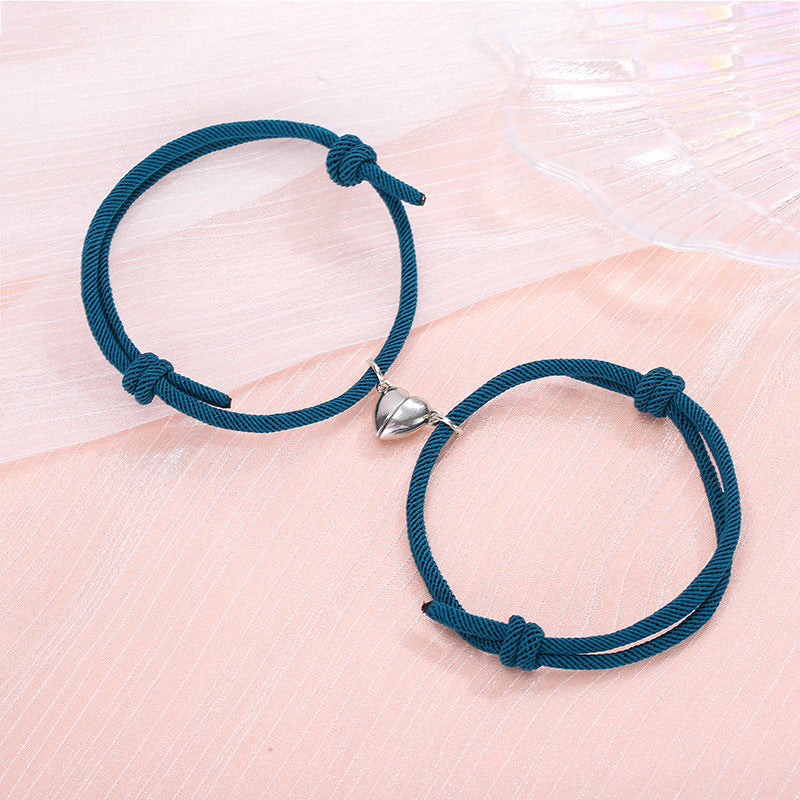 Two blue braided bracelets with silver heart-shaped clasps on a light pink surface.