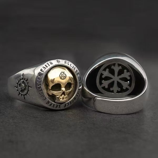 Silver ring with gold skull design on a dark background