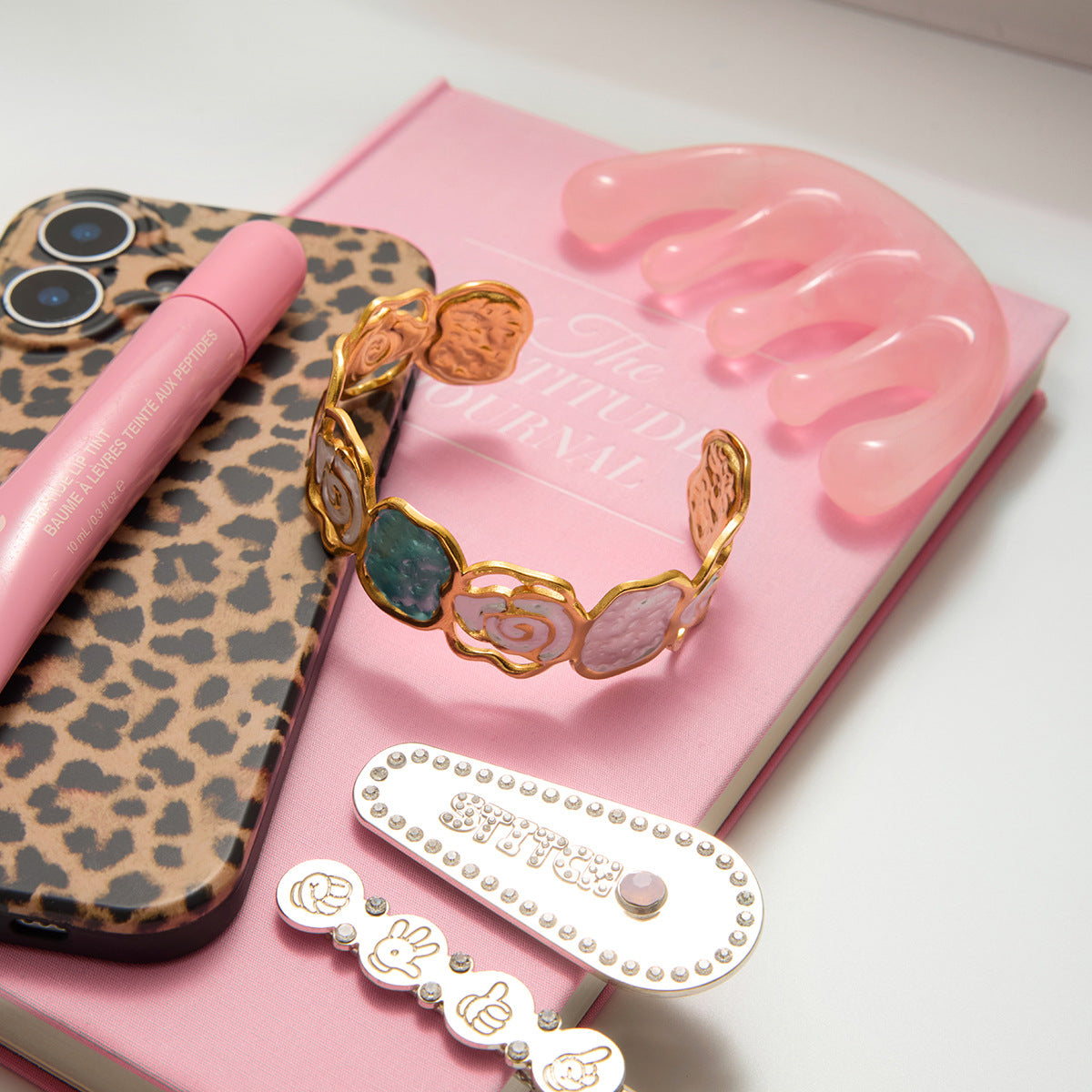 Phone case with leopard print pattern, pink hairbrush, and decorative hair accessories on a pink background