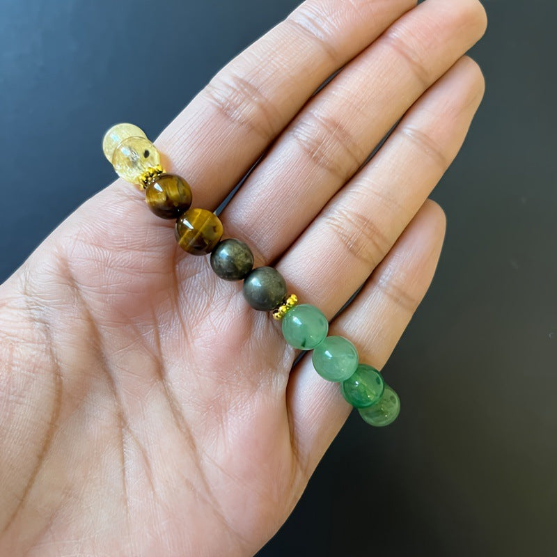 Hand holding a bracelet with green and brown beads against a dark background