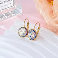 Gold earrings with multicolored gemstones on a white card with a pink floral background