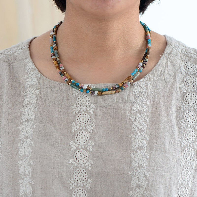Necklace with multicolored beads worn by a person in a light gray embroidered top.