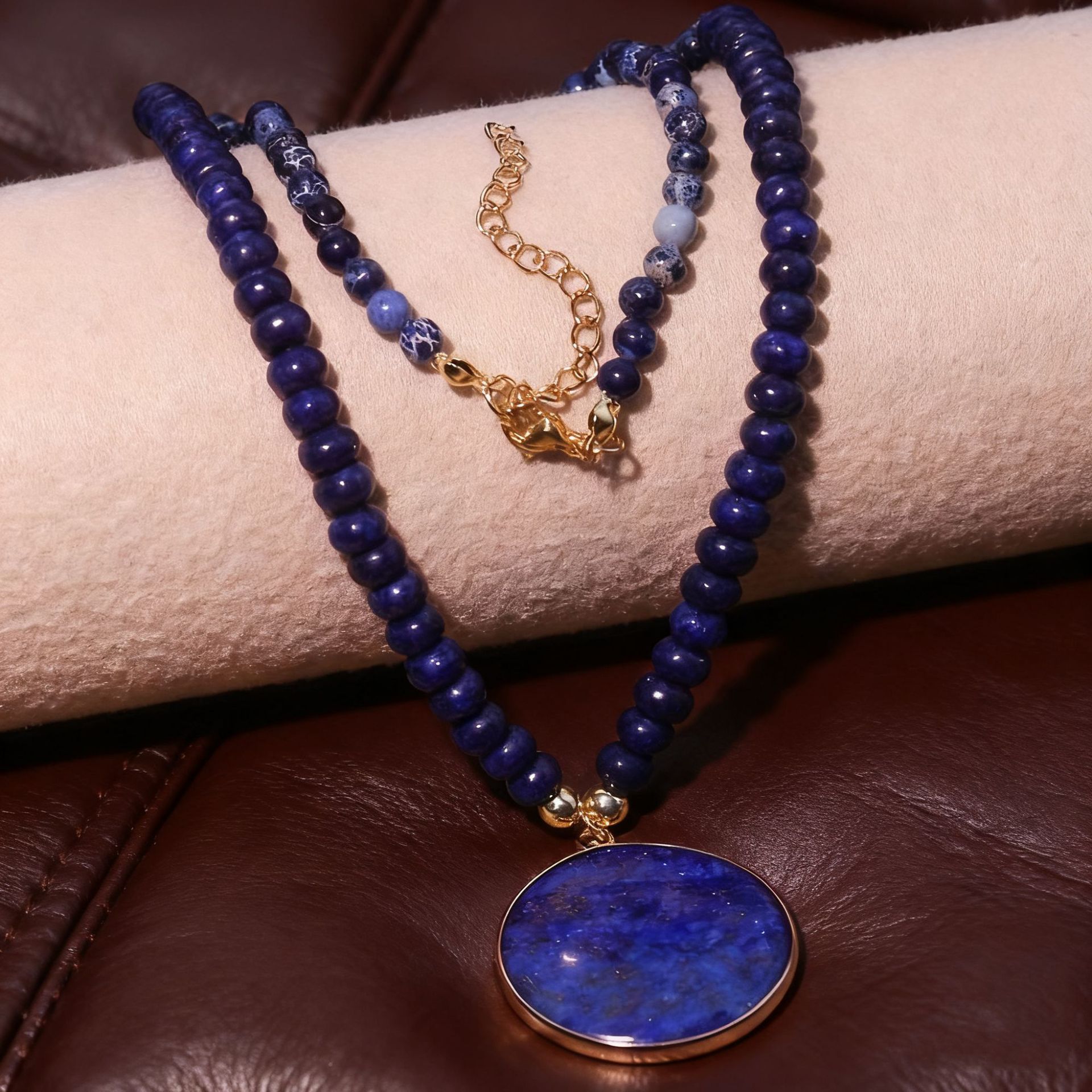 Blue beaded necklace with a gold clasp on a person's wrist against a brown leather background