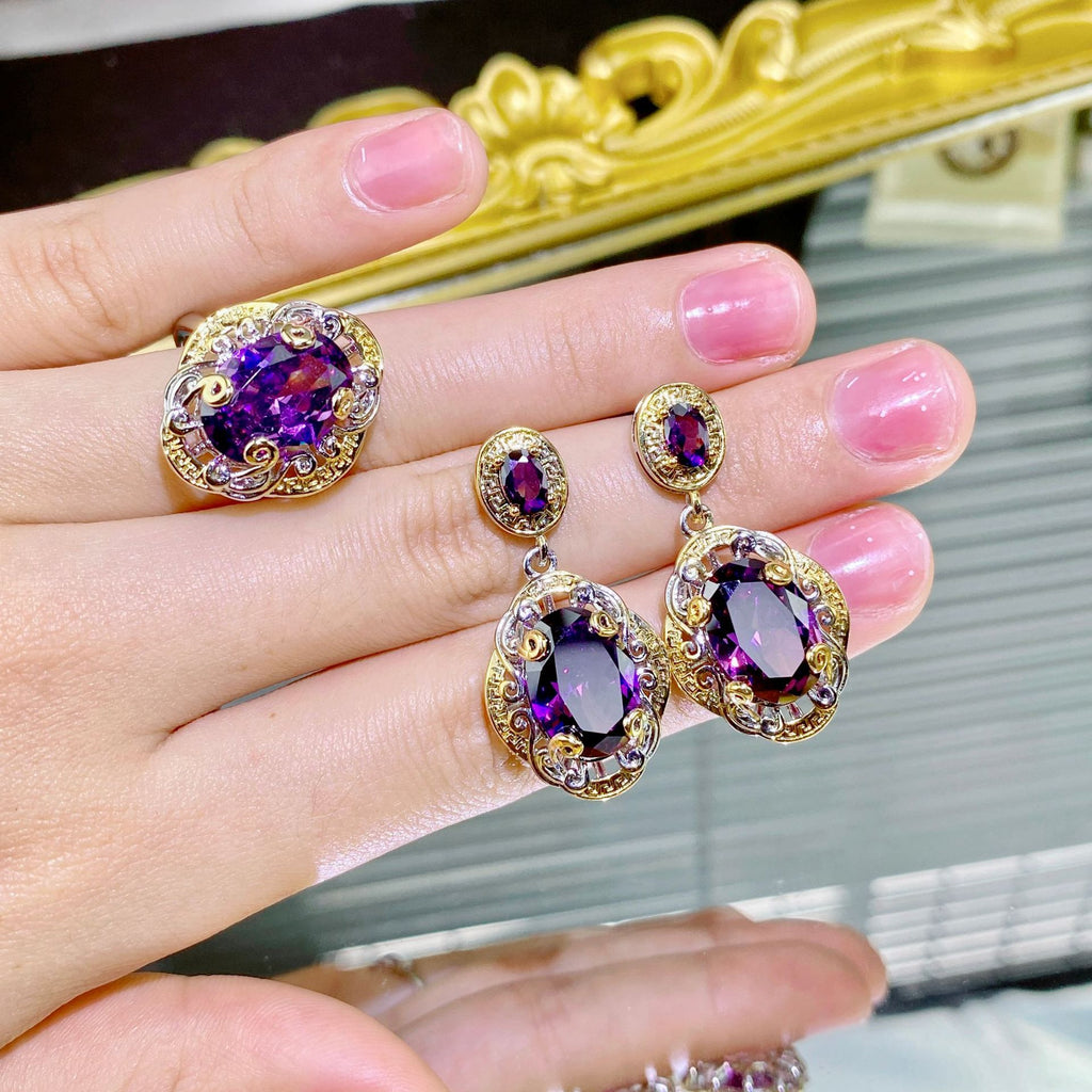 Purple gemstone earrings on a hand with a decorative mirror in the background