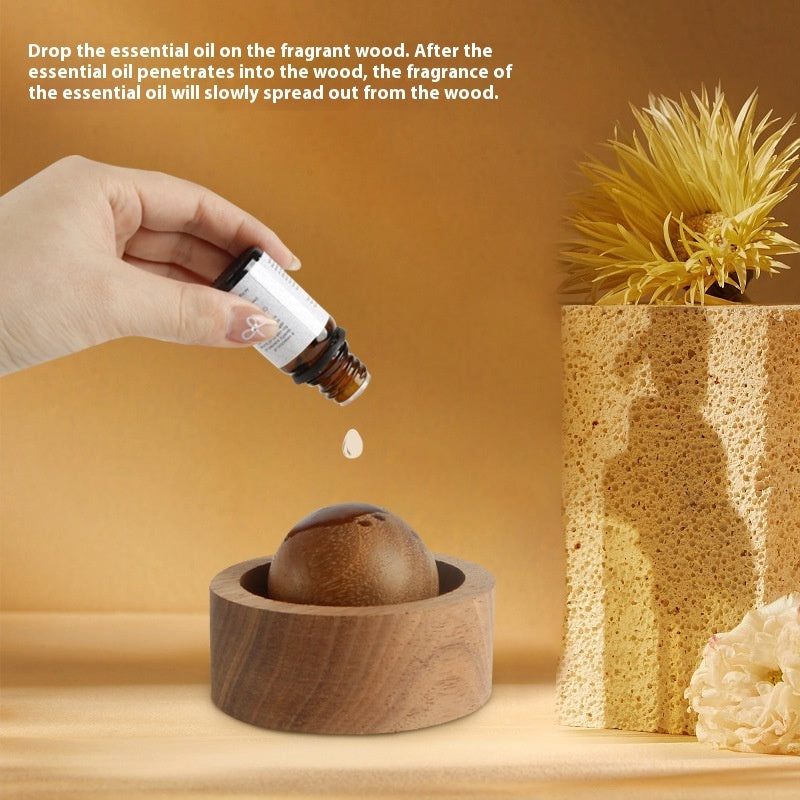 Hand dropping essential oil onto a wooden diffuser with a decorative plant in the background.