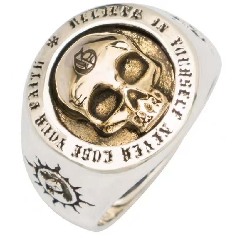 Gold and silver ring with skull design and engraved text on a white background