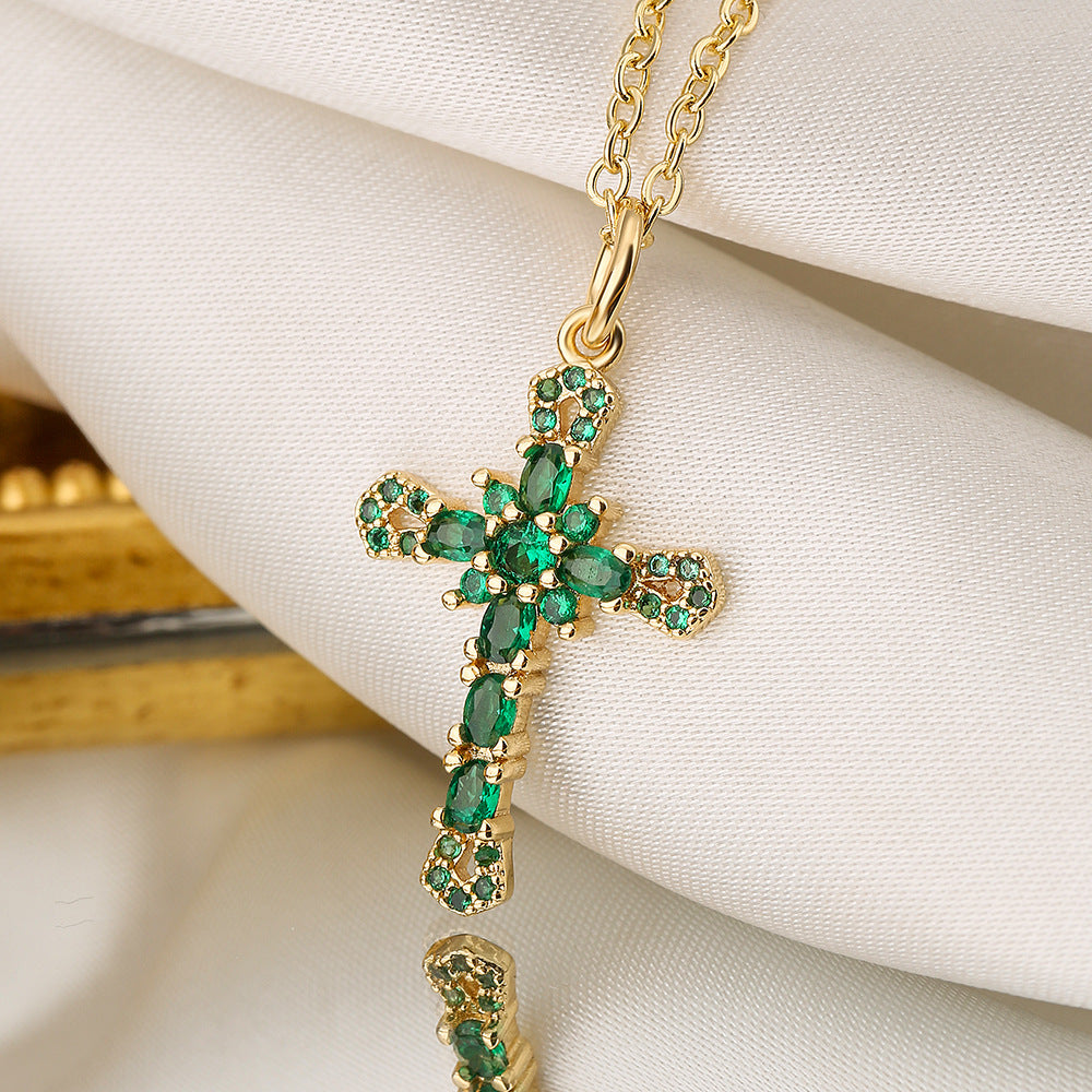 Gold cross necklace with emerald stones on a white fabric background