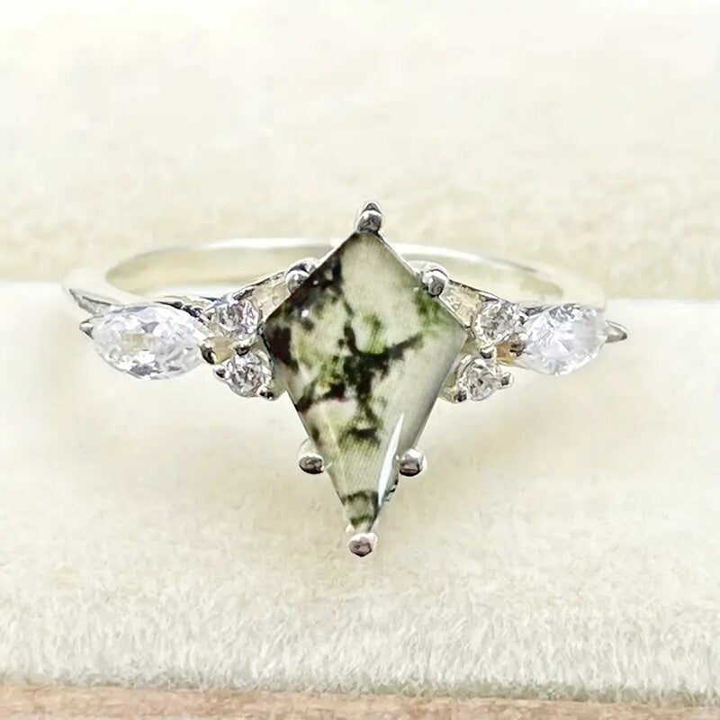 Ring with a green gemstone and clear stones on a white background