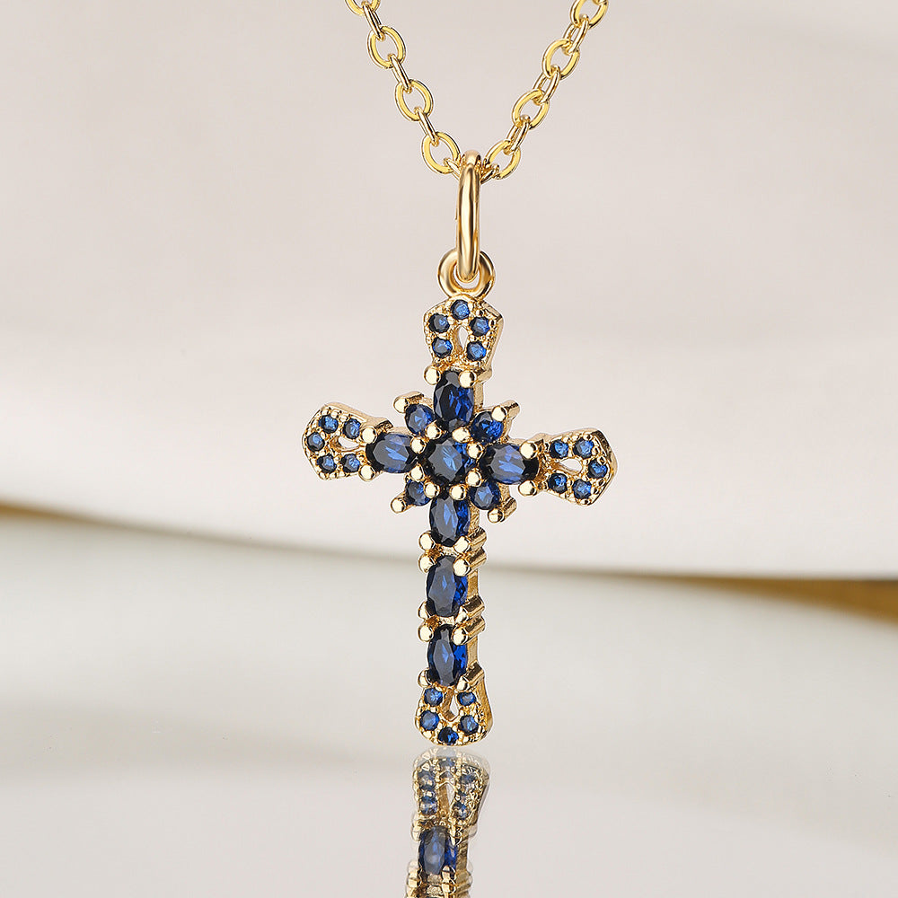 Gold cross pendant with blue stones on a gold chain against a light background