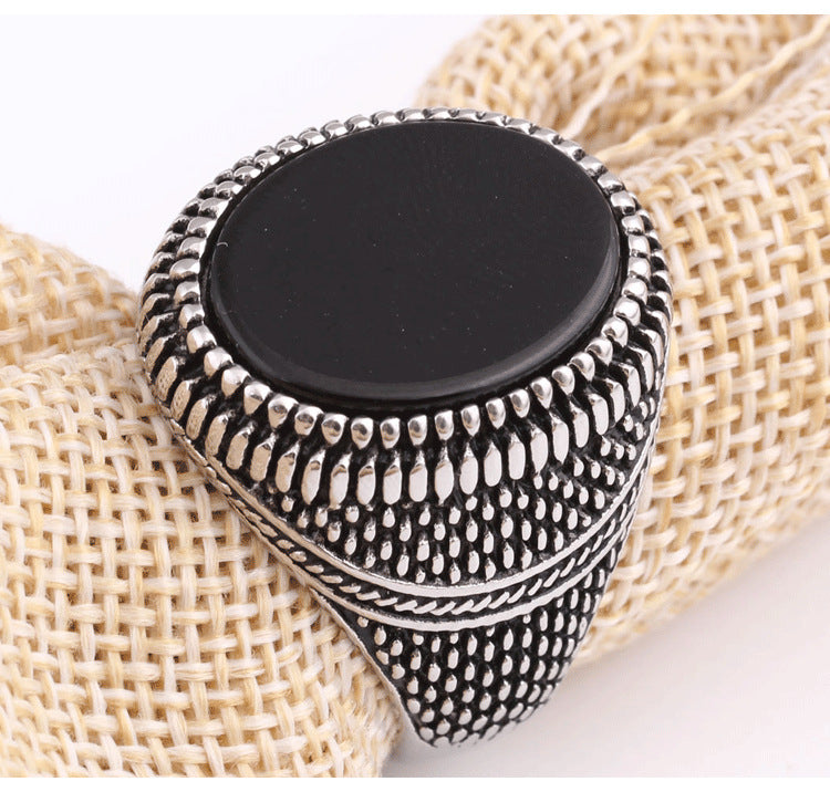 Silver ring with a black stone on a textured beige surface