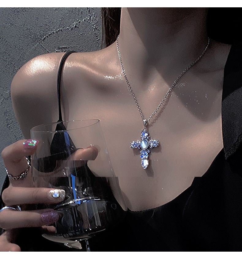 Person wearing a silver necklace with a cross pendant, holding a glass.