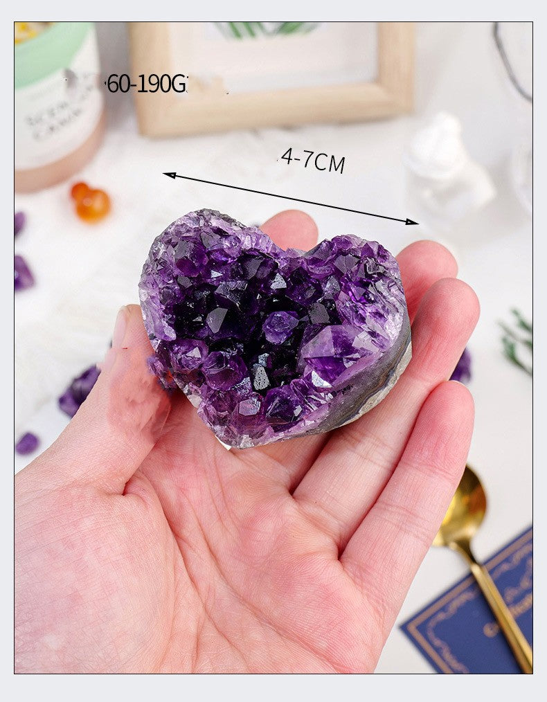 Heart-shaped purple crystal held in a hand with measurements indicated