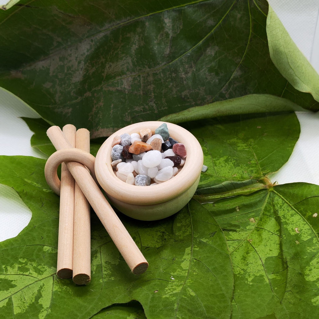 Small bowl with stones and two wooden sticks on green leaves