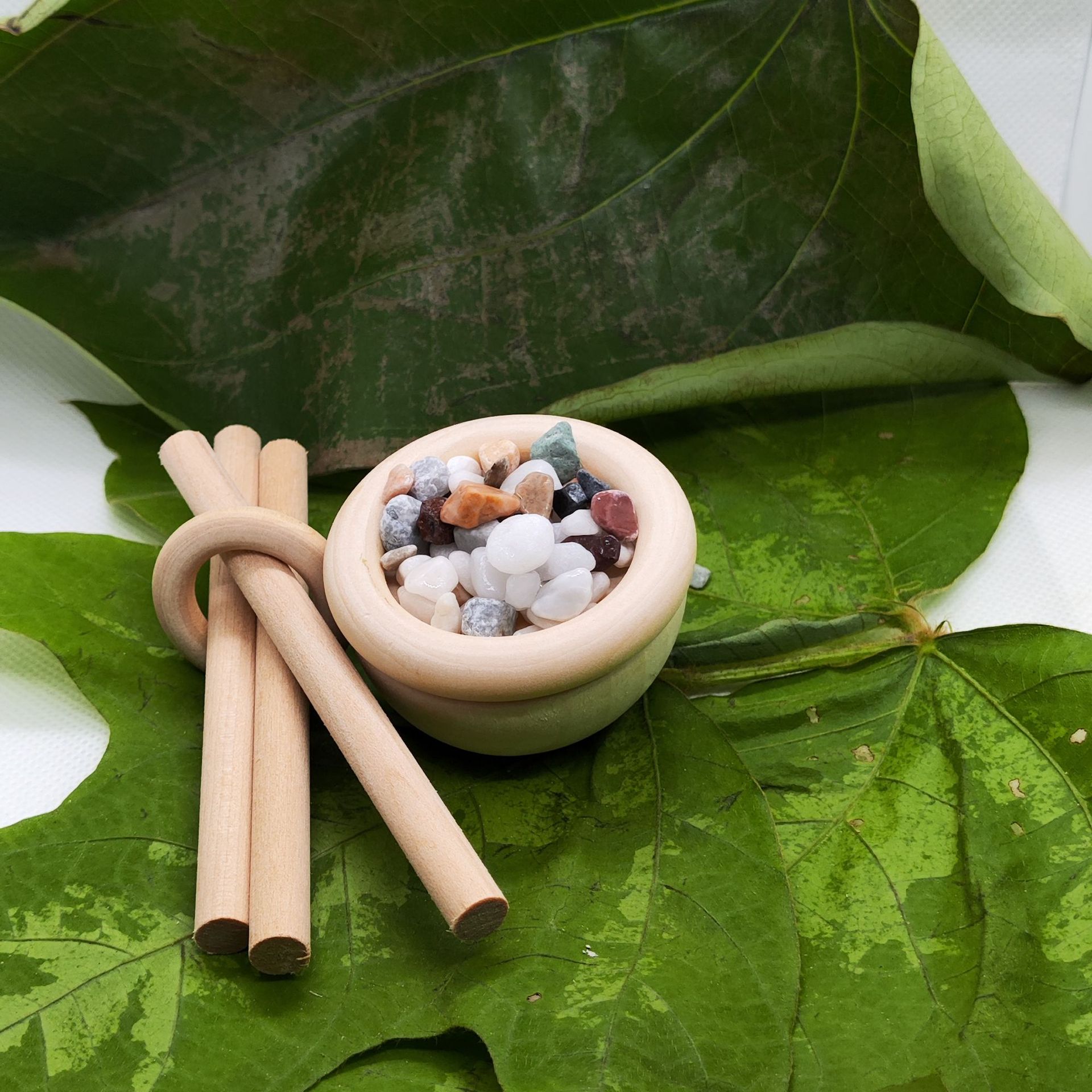 Small bowl with stones and two wooden sticks on green leaves
