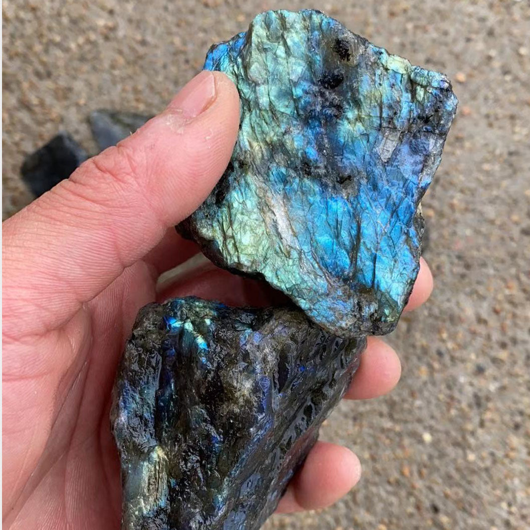 Hand holding two labradorite crystals with a reflective, multicolored surface.