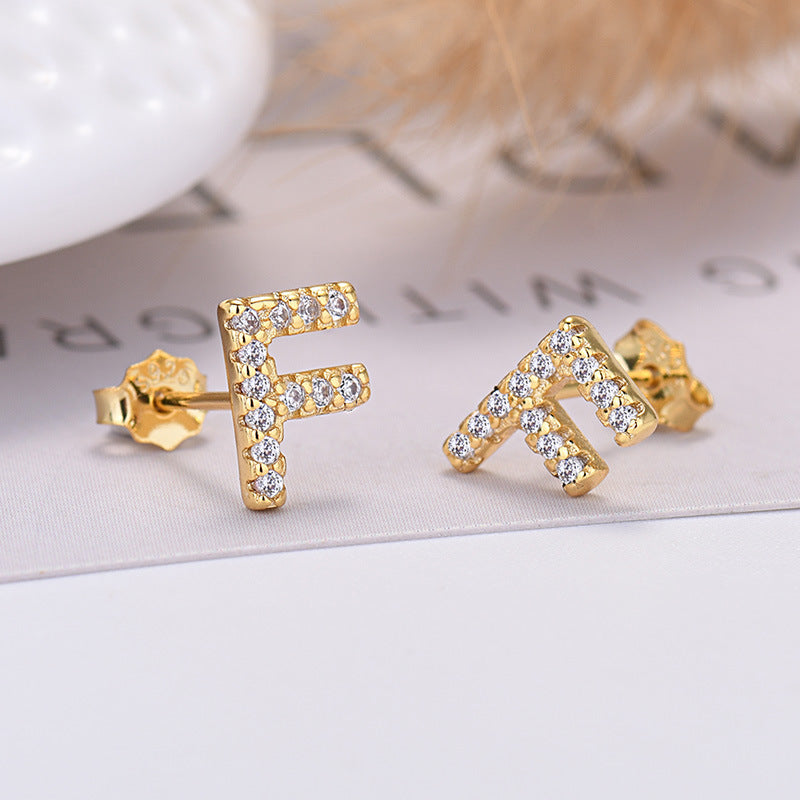 Gold letter 'F' and 'M' earrings on a light background