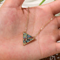 Gold necklace with a colorful triangle pendant held in a hand.