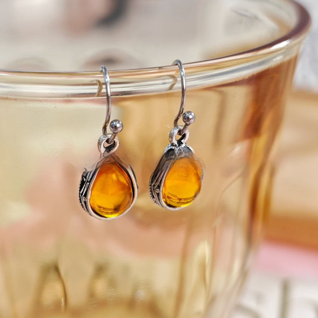 Amber teardrop earrings with silver hooks on a glass of tea.