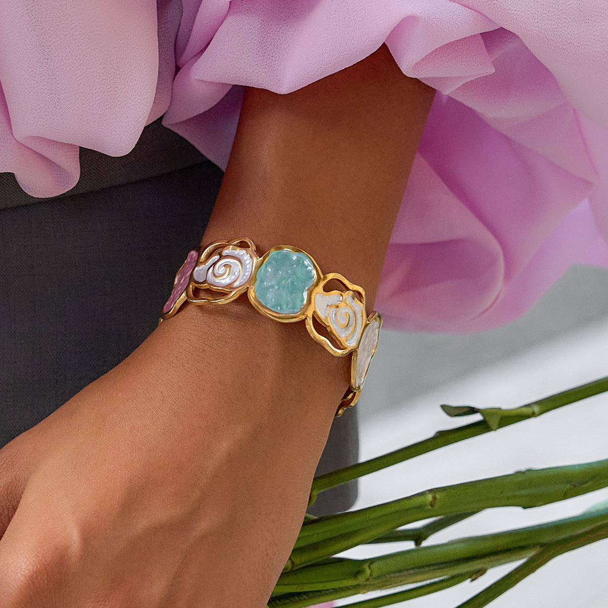 Close-up of a wrist wearing a gold bracelet with colorful stones, against a blurred background.