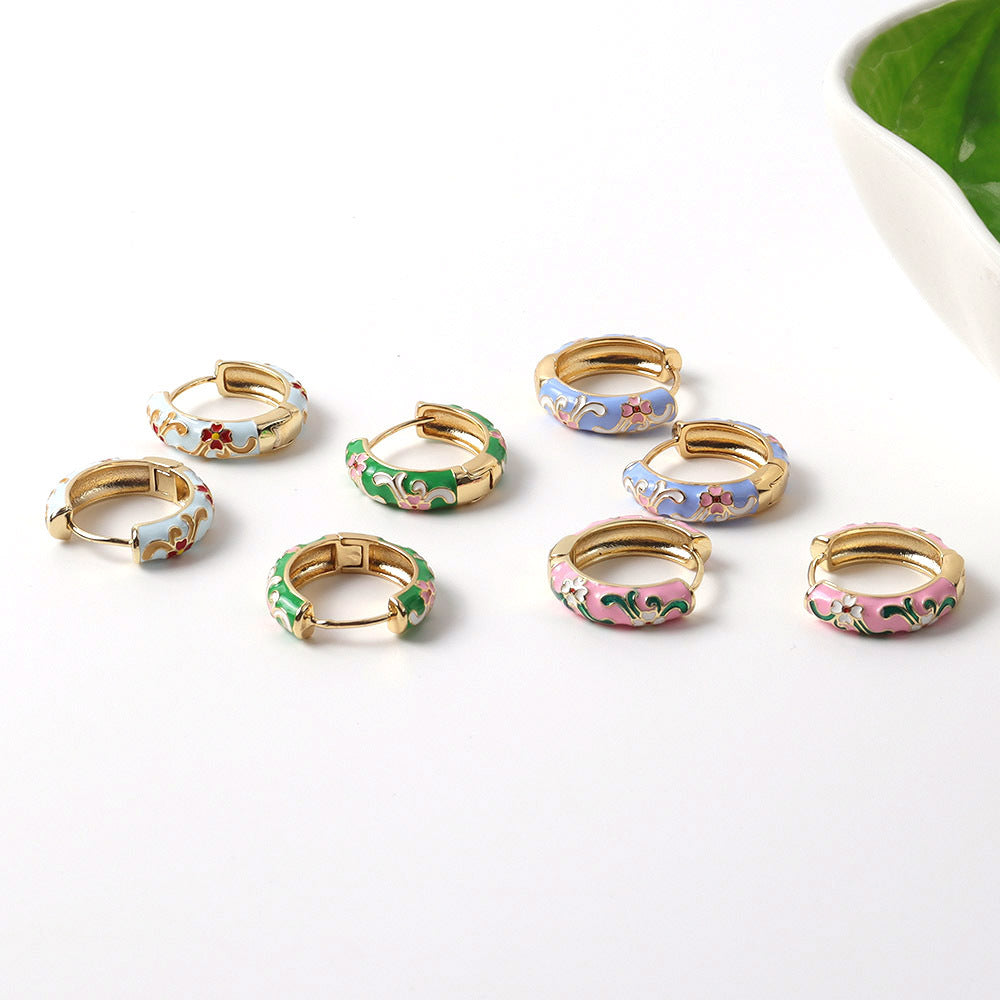 Set of small hoop earrings with colorful enameled designs on a white surface.