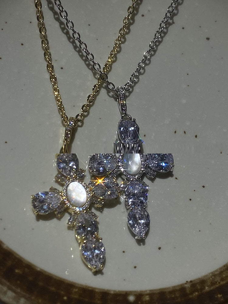Cross-shaped pendant with gemstones on a chain against a neutral background