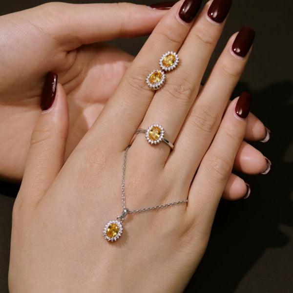 Hand wearing a ring and necklace with yellow gemstones on a dark background