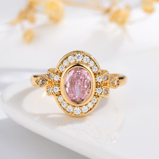 Gold ring with a pink gemstone and diamond accents on a white surface.