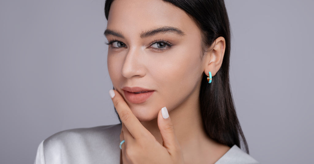 Woman with dark hair and earrings against a gray background