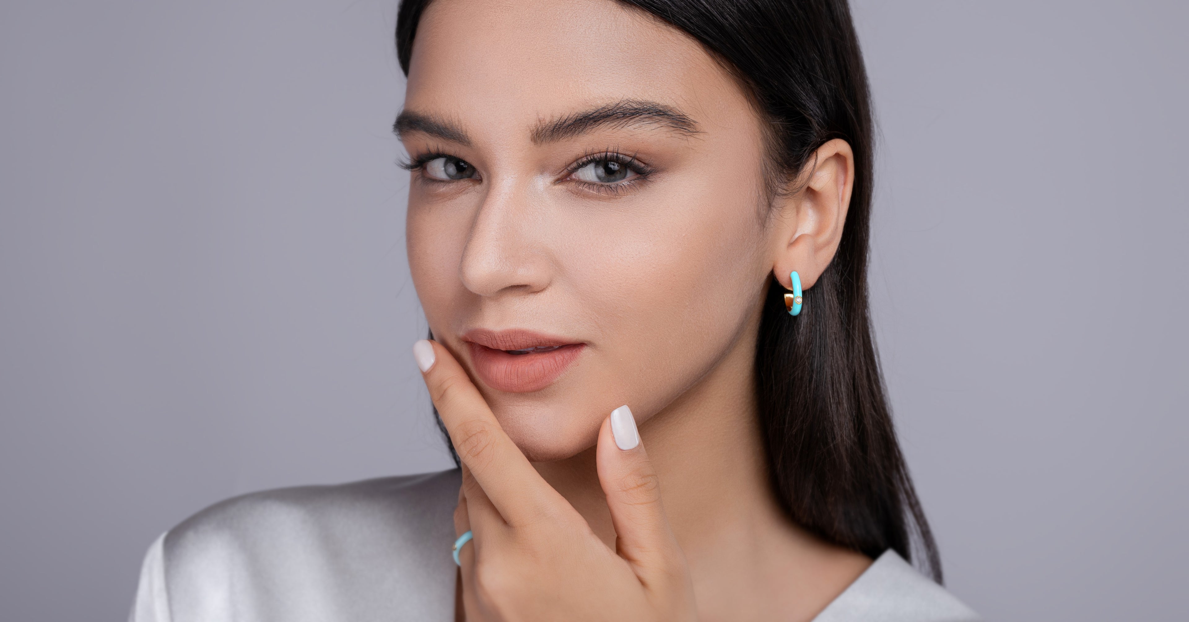 Woman with dark hair and earrings against a gray background