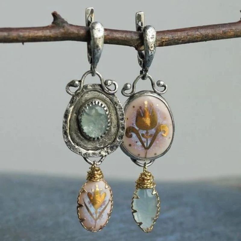 Pair of earrings with intricate designs and gemstones hanging on a branch.