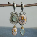 Pair of earrings with intricate designs and gemstones hanging on a branch.