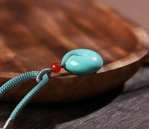 Turquoise pendant with a red bead on a wooden surface