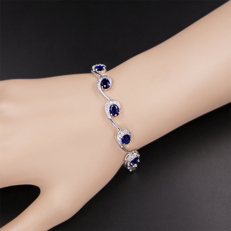 Silver bracelet with blue gemstones on a wrist against a dark background