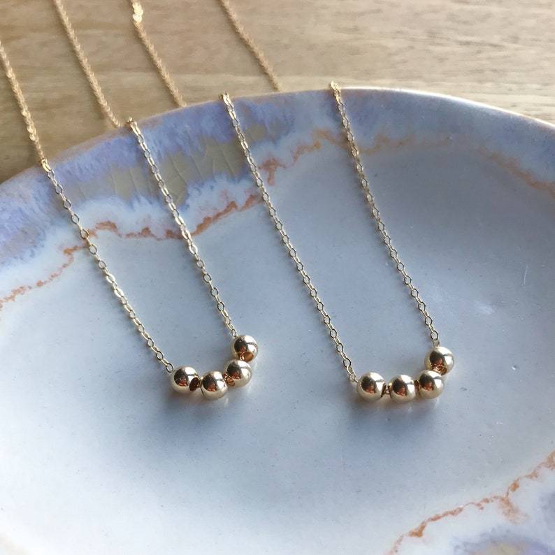 Two gold necklaces with small beads on a ceramic plate