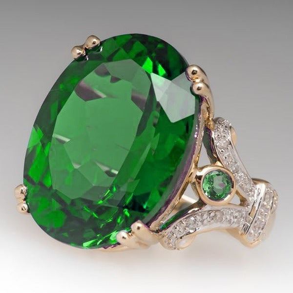 Gold ring with a large green gemstone and smaller green gemstones on a gray background