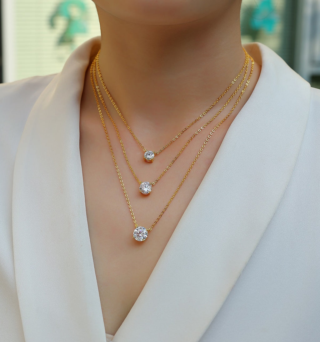 Gold necklaces with diamond pendants on a mannequin wearing a white outfit.