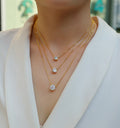 Gold necklaces with diamond pendants on a mannequin wearing a white outfit.