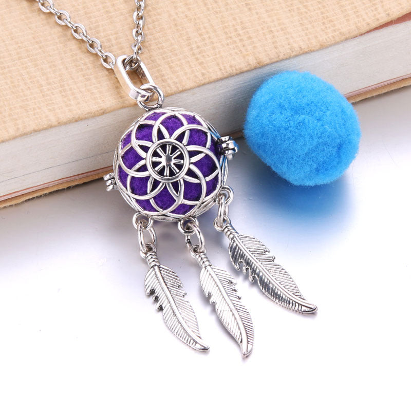 Necklace with a purple pendant and feather charms on a white surface.