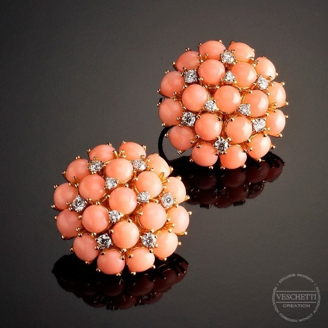 Pair of coral and diamond earrings on a reflective surface with 'Veschetti Creation' branding.