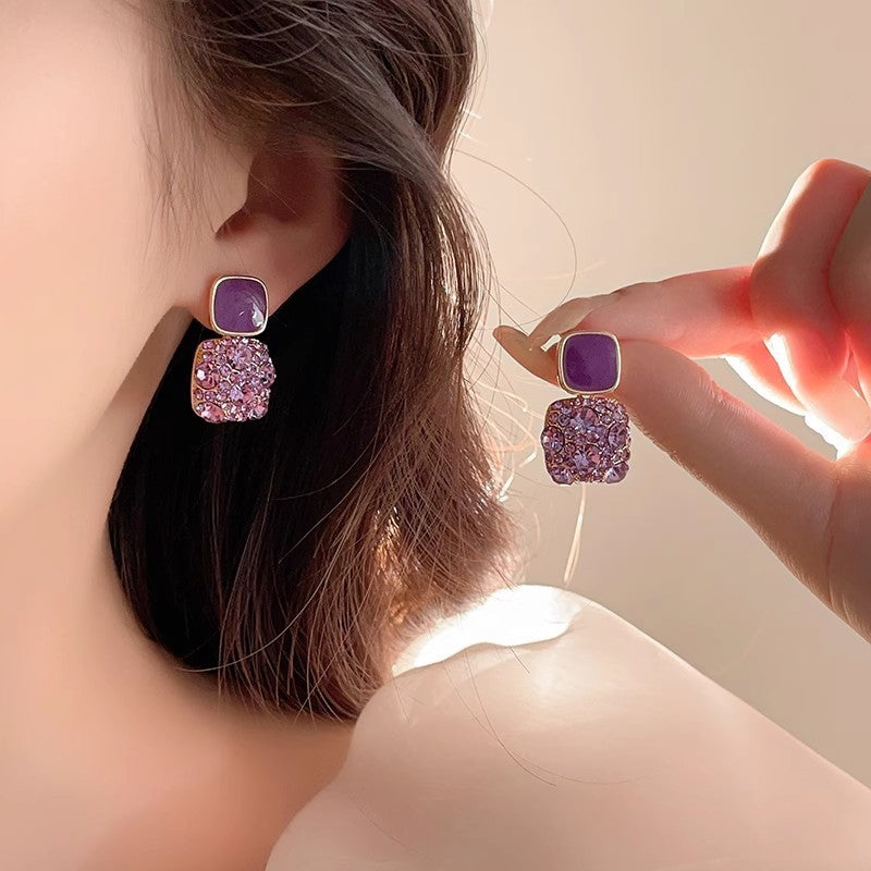 Purple and pink earrings being worn and held by a person